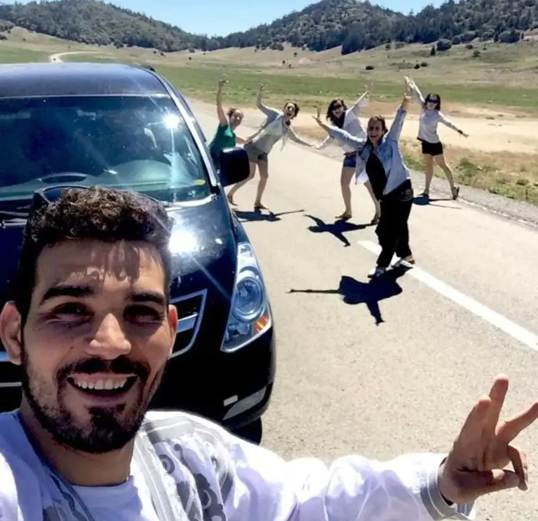 Chauffeur avec un groupe de voyageuses près du minivan, sur une route de montagne
