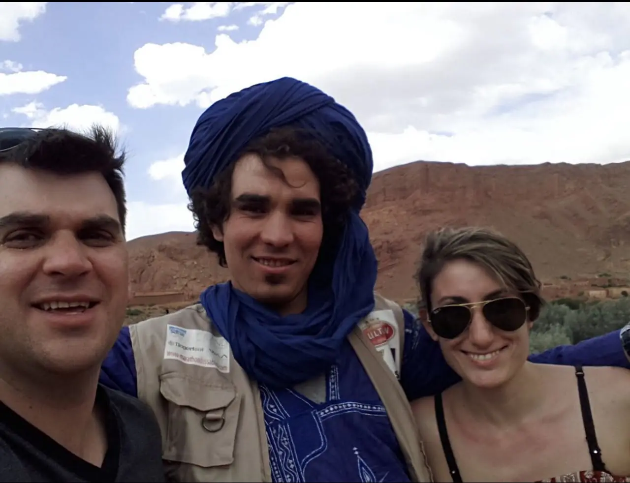 Due viaggiatori con un uomo con il turbante blu, con montagne rosse alle spalle
